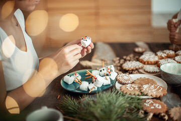 Mom and children decorate Christmas gingerbread at home. A boy and a girl paint with cornets with sugar icing on cookies. New Year's decor, branches of a Christmas tree.
