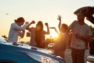 A group of young women and men dancing to music having a good time together outside on a parking...