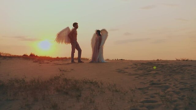 dark silhouette two angles meet at sunset. Lovers muscular man and tender woman marry in heaven. concept love fidelity. orange sky sun light. Costume white wings. Fantasy couple girl and guy in love