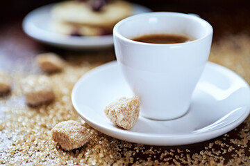 Cup of coffee and brown sugar (focus on sugar) on wooden background. Close up. 
