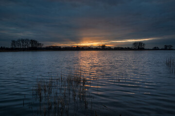 Sunset over a quiet lake and dark clouds in the evening