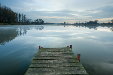Fototapeta premium Wooden bridge towards a misty and calm lake