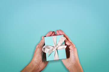 hands holding a turquoise gift boxe tied with white silk ribbon. Suitable for concepts like luxury gift, anniversary, Valentine's day, Mother's day or christmas. Copy space available