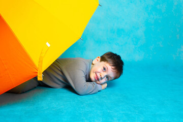 A boy with a colored umbrella on a blue background . Summer season. Umbrella from the rain. Boy on a blue background. Bright multi-colored umbrella. Copy space. The boy and the umbrella . Article © alenka2194