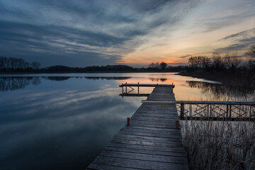 Long wooden bridge on the lake and sunset clouds