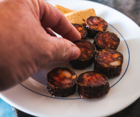 Scene inside a typical Spanish family home eating a tapa of chorizo pork sausage while holding a piece of black pudding.