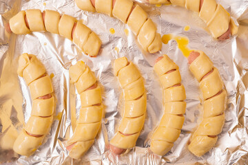 Cooking sausages in dough. Sausages wrapped in raw yeast dough lie on a baking sheet