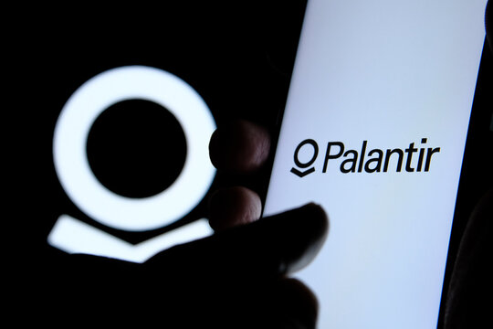 Stafford / United Kingdom - November 18 2020: Palantir company logo on the screen of smartphone, finger touching it and the blurred Palantir logo on the background.