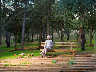 Fototapeta premium Pretty young woman wearing long dress and sitting in a park with cheerful fitness