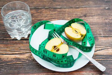 On the plate there is a centimeter and an apple cut in half and a fork in the middle, next to it is a glass of water.