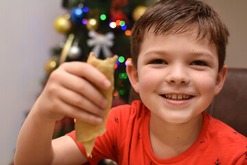 Little boy eating pancakes in front of traditional Christmas tree. Child enjoy eating pancake in Christmas Eve holiday celebration