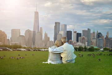 Senior couple sitting on green meadow against New York cityscape