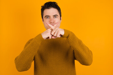 Young handsome Caucasian man wearing yellow sweater against orange wall has rejection angry...