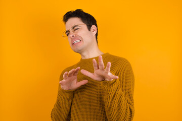 Ugh how disgusting! Displeased Young handsome Caucasian man wearing yellow sweater against orange...
