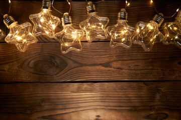 Bright luminous Christmas garlands in the shape of stars lie on a dark wooden background.