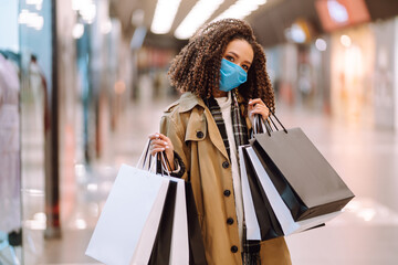 Young woman in protective medical mask  make purchases in a shopping center,  go shopping. Trade, buyers, black friday, discounts, sale concept. Shopping in the coronavirus epidemic.