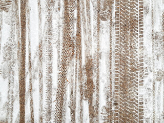 Fototapeta premium Different wheels and shoes prints on road surface covered with thin layer of snow. Shared-use paths for cyclists and pedestrians. Vertical lines background.