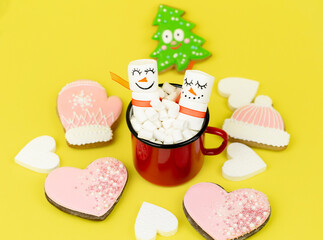 marshmallow snowmen in a red coffee Cup, surrounded by Christmas decorations on a yellow background