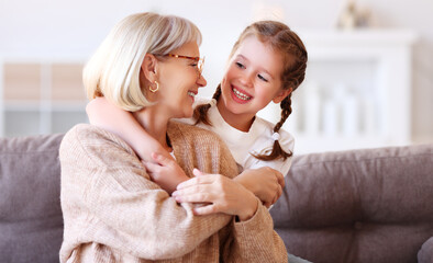 Happy grandmother and granddaughter hugging on sofa.