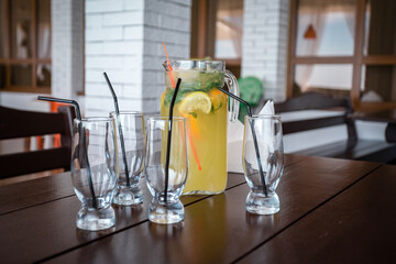Refreshing lemonade with orange and mint in a decanter on a table surrounded by glasses