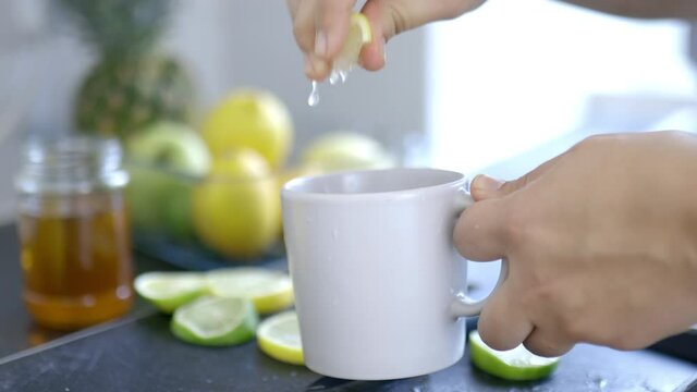 Female hands holding a cup and squeezing a lemon into it