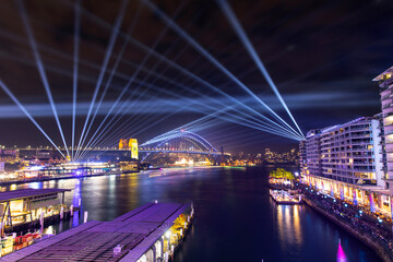 Sydney Harbour at night with beaming lights in the sky for Vivid Festival. 