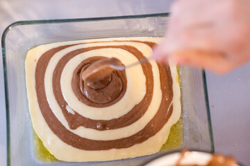 Raw dough for a sweet zebra pie in a baking dish and ingredients for it. Cooking process.