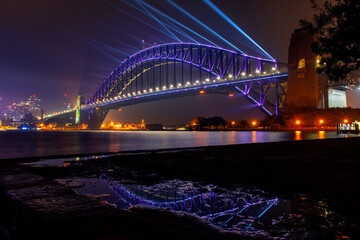Sydney Harbour Bridge at night with beaming lights for Vivid Festival. View from Kirribilli puddle