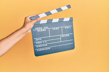 Hand of hispanic man holding movie clapboard over isolated yellow background.