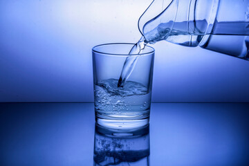 Pouring water from jug into glass on blue background