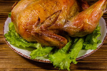 Plate with roasted whole chicken and lettuce leaves on a wooden table