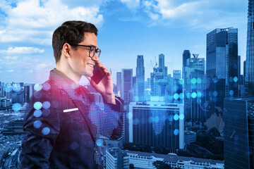 A young handsome eastern businessman processing conference call to develop social media marketing strategy to achieve business goals. Hologram icons over Singapore background.