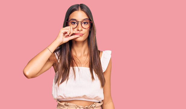 Young hispanic woman wearing casual clothes and glasses mouth and lips shut as zip with fingers. secret and silent, taboo talking