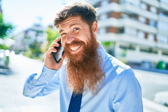 Young handsome redhead businessman smiling happy. Standing with smile on face having conversation talking on the smartphone at street of city.