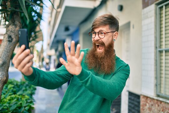 Young irish man with redhead beard smiling happy and doing video call using smartphone at the city.