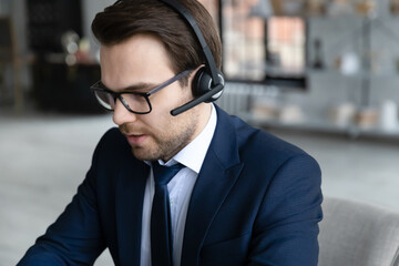 Close up confident businessman wearing glasses and headset consulting client online, focused...