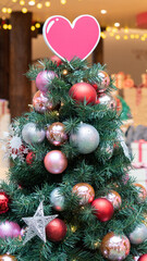 One lovely Christmas tree with the sweet pink heart on top and many balls and star. The festive decoration and colorful ornaments.