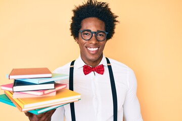 Handsome african american nerd man with afro hair holding books looking positive and happy standing and smiling with a confident smile showing teeth