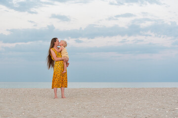 Young mother gently hugs her daughter and kiss. Mom and baby on sea background