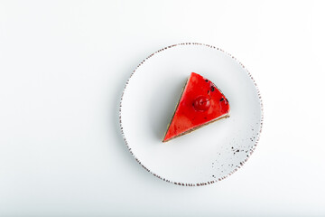 Piece of cake with red jelly frosting and maraschino cherry on white plate. Top view