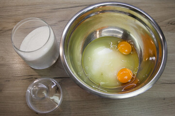 White sugar and two eggs in a metallic bowl on the wood background. the second step for making muffins, pie, biscuit. baking process step by step. prepare cake for sweetheart on valentine's day