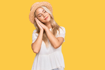 Young blonde girl wearing summer hat sleeping tired dreaming and posing with hands together while smiling with closed eyes.