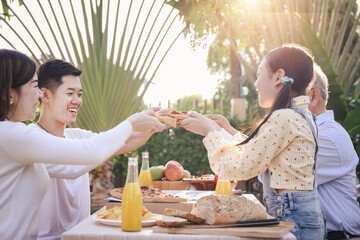 Happy asian family having enjoying meal(pizaa, salad,snack, orange juice) together in home garden. Outdoor dinner party in holiday. Multi generation family concept.