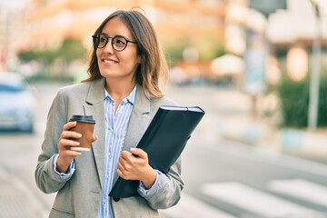 Young hispanic businesswoman drinking coffee holding binder at the city.