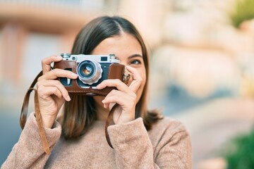 Young hispanic tourist woman smiling happy using vintage camera at the city.