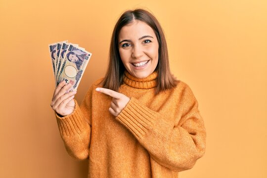 Young woman holding 5000 japanese yen banknotes smiling happy pointing with hand and finger