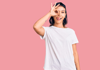 Young woman wearing casual clothes doing ok gesture like binoculars sticking tongue out, eyes looking through fingers. crazy expression.