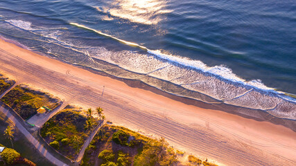 Aerial view over Gold Coast Main beach and ocean with palm trees and sunrise light.