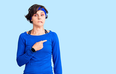Beautiful young woman with short hair wearing training workout clothes pointing aside worried and nervous with forefinger, concerned and surprised expression