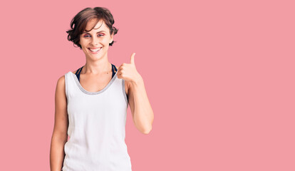 Beautiful young woman with short hair wearing casual sport clothes smiling happy and positive, thumb up doing excellent and approval sign